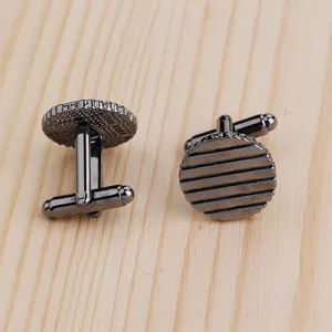 Détail de boutons de manchette ronds en métal gris fusil avec texture rayée sur bois