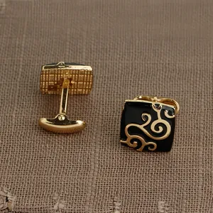 Détail de boutons de manchette carrés dorés avec émail noir et motifs floraux gravés