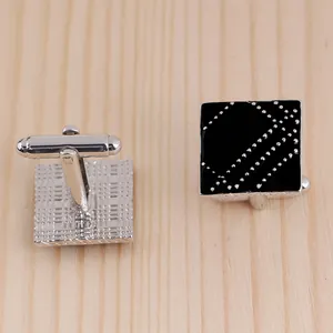 Detail of square black enamel cufflinks with silver diagonal striped dots on wood