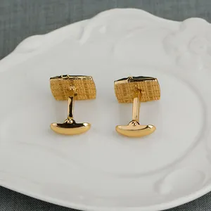 Paire de boutons de manchette carrés dorés avec texture quadrillée sur plat blanc