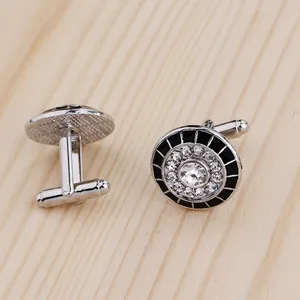 Detail of round silver cufflinks with black enamel and sparkling rhinestones on wood