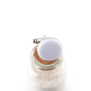 Detail of round silver cufflinks with white face on a glass bottle with sand