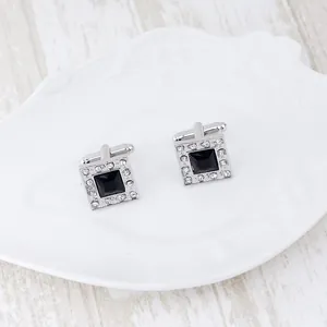 Detail of silver square cufflinks with black gemstone and white crystal inlay on white dish