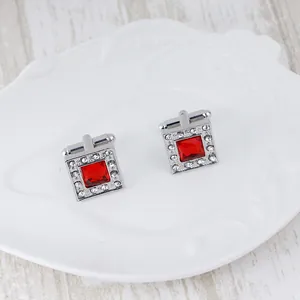 Square silver cufflinks with central red crystal and white rhinestones on a white plate