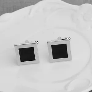 Polished silver square cufflinks with black enamel inlay on an elegant white ceramic plate