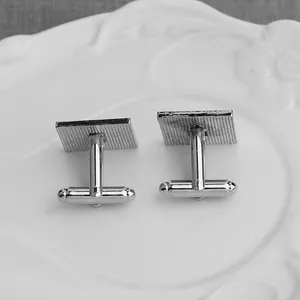 Silver square cufflinks with grid texture and T-bar closure on a white porcelain plate