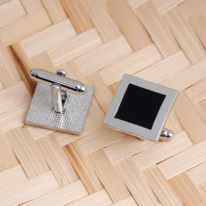 Detailed view of silver square cufflinks with black enamel inlay on a textured background