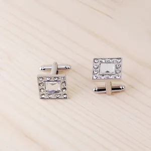 Macro detail of silver square cufflinks with crystal stone inlay on wood background