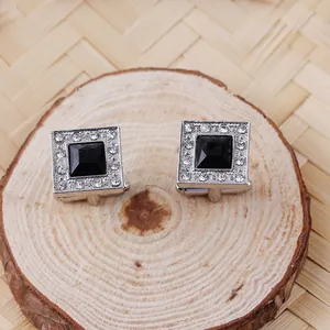 Macro detail of silver cufflinks with square black gemstone and crystal trim on wood