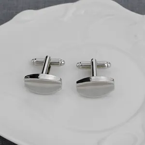 Silver geometric cufflinks with a central groove, displayed on a textured white plate