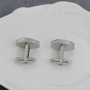 Close-up of silver square-patterned cufflinks with toggle closure on a ceramic tray