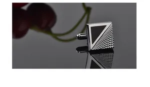 Macro view of square alloy cufflinks featuring black enamel and geometric grid texture