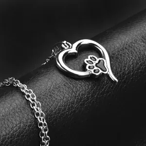 Silver hollow heart necklace with black paw print pendant on black leather background