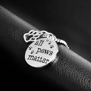 Macro shot of silver stainless steel pendant engraved with All Paws Matter and paw print