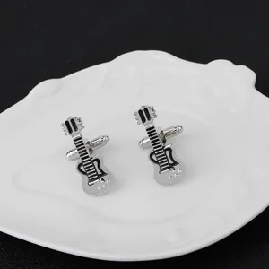 Macro shot of silver guitar cufflinks with black enamel on an ornate white ceramic plate