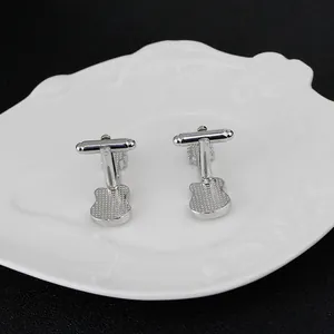 Elegant silver guitar-shaped metal cufflinks for men's shirts on a textured white plate