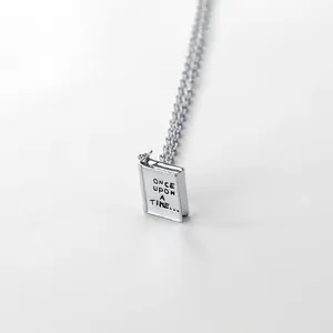Minimalist silver book pendant necklace with Once upon a time engraving on gray background