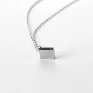 Detailed macro view of a silver square book pendant on a fine cross chain necklace
