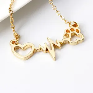 Golden heart EKG necklace with paw print pendant on white ceramic background