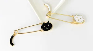 Detail of cute cat safety pins with enamel drips and dangling tails in black and white
