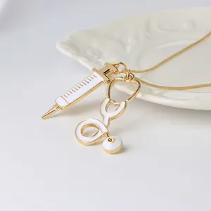 Collier médical doré avec pendentifs seringue et stéthoscope sur une assiette blanche