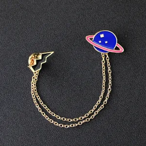 Detail of enamel planet and lightning brooch with gold chains on black background