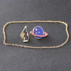 Close-up of enamel planet and lightning pins with golden chain on textured grey base
