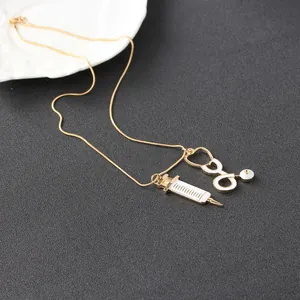 Détail du pendentif seringue et stéthoscope avec émail sur une chaîne dorée fine