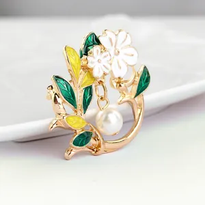 Detail of floral enamel brooch with green leaves and a round white hanging pearl