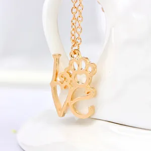 Detailopname van gouden ketting met LOVE-letters en pootafdruk hanger op wit keramiek decor