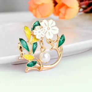 Elegant gold flower brooch with white petals, green leaves, and a hanging faux pearl