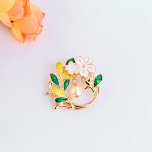 Detail of floral brooch featuring gold leaves, green enamel, and a hanging white pearl