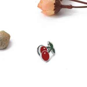 Close-up of red cherry enamel charm with green leaves on white background