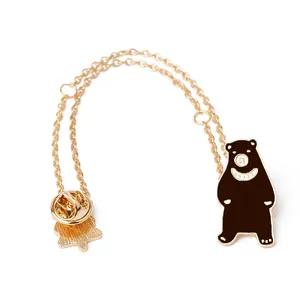 Détail d'une broche ours dessin animé avec chaîne dorée et émail noir sur fond blanc