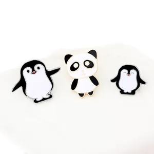 Close-up of three cute enamel pins featuring panda and penguins in black and white finish