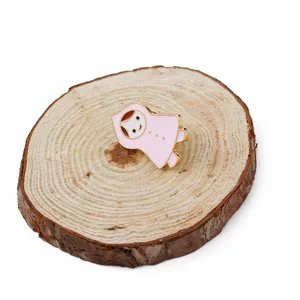Détail de broche en émail rose motif fille sur un socle en bois naturel