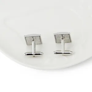 Silver cufflinks with blue stripes and grid texture shown on a white ceramic background