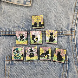 Set of eight black cat tarot enamel pins displayed on a blue denim jacket pocket