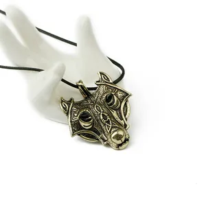 Close-up of bronze Viking wolf head pendant with Nordic runes on a white hand model