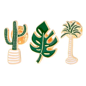 Three enamel plant pins set including cactus, monstera leaf, and palm tree with gold trim