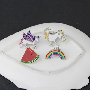 Close-up of four enamel pins with unicorn and rainbow designs on white ceramic plate