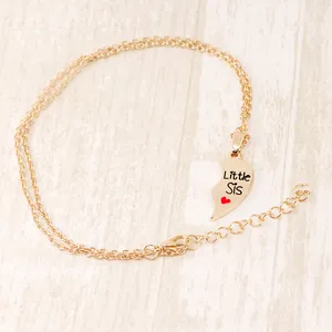 Detail of golden Little Sis half heart pendant necklace with red heart on wood background