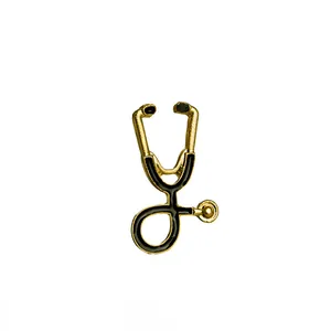 Détail d'une broche stéthoscope dorée avec émail noir sur fond blanc minimaliste