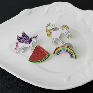 Cartoon enamel pin set with unicorn, rainbow, and watermelon designs on a ceramic plate