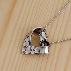 Gros plan d'un pendentif cœur ruban à mesurer en argent vintage sur fond bois clair