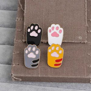 Close-up of four colorful cat paw enamel brooches with pink pads on velvet