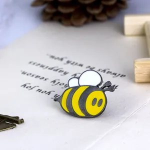 Detailed view of cartoon bee enamel brooch with yellow and black stripes on white card