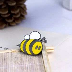 Macro shot of an enamel bee brooch with yellow stripes and white wings on a woven mat