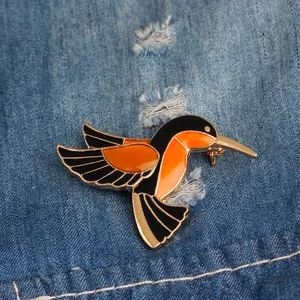 Dettaglio di una spilla a colibrì arancione e oro su sfondo di tessuto denim blu