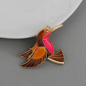 Dettaglio di una spilla a colibrì con ali in smalto colorato e cornice in metallo dorato